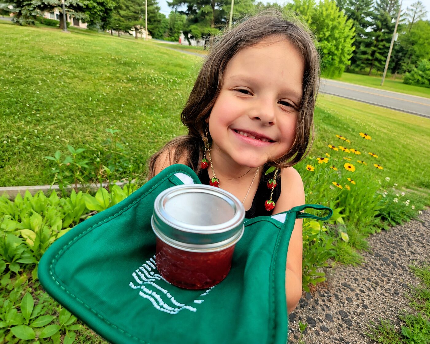 Young girl in a garden holding a jar of jam she made and preserved herself